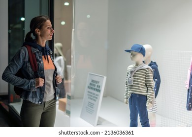 Young Woman Stands Near Kid's Wear Store Window.