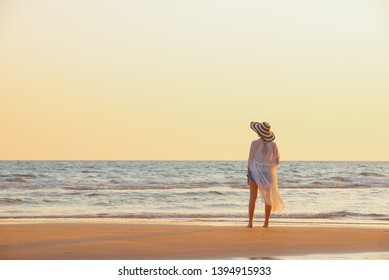 A young woman stands on the beach during a sunset, summer vacation. - Shutterstock ID 1394915933