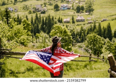 A young woman stands on a mountain and holds the US flag in her hands. American Independence Day celebration.