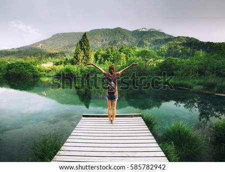 Young woman stands on a wooden bridge with raised arms up on the nature background. Travel, Freedom, Lifestyle concept. Slovenia, Europe.