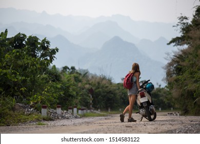 Young woman stands with the scooter on the empty lonely road with mountains on the background - Powered by Shutterstock