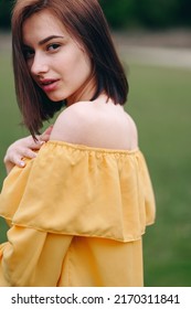 A Young Woman Stands Sideways In A Yellow Blouse. Hair Covers Half Of The Face. Soft Blurred Background. Advertising Cosmetics. Facial Skin Care