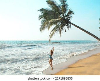  Young Woman Stands Under A Palm Tree On The Beach . The Concept Of Vacation And Travel To The Ocean. Resort On The Island. Beach Photo, Paradise Vacation On The Beach