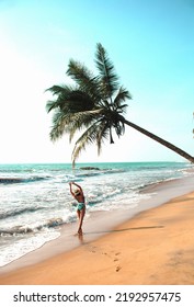  Young Woman Stands Under A Palm Tree On The Beach . The Concept Of Vacation And Travel To The Ocean. Resort On The Island. Beach Photo, Paradise Vacation On The Beach