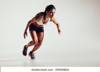 Young Woman Starting To Run And Accelerating Over Grey Background. Powerful Young Female Athlete Running In Competition.