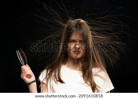 Young woman with static long hair and hair brush, on black background. 