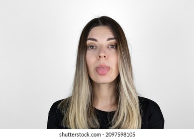 Young woman sticking out tounge, close up portrait. Teasing you through camera while isolated with white background. 