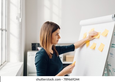 Young Woman Sticking Yellow Sticky Notes To Flip Chart At Office