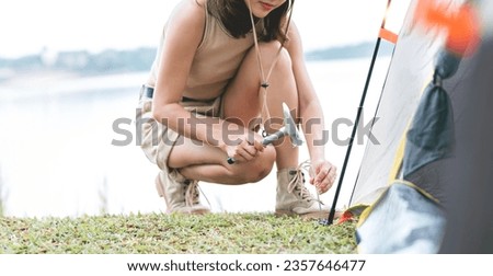 Young woman  sticks a metal tent peg into the ground. Setting up a tent for camping.