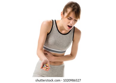 young woman with stomachache holding pills isolated on white