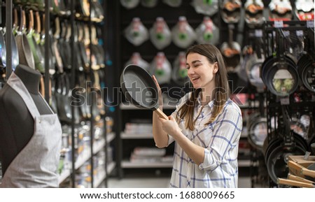 A young woman in the store chooses a frying pan . The concept of shopping for a home.