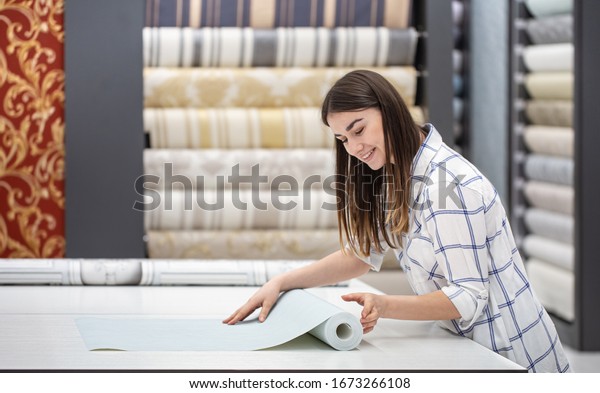 A young woman in a store chooses\
Wallpaper for her home. Concept of repair and\
shopping.