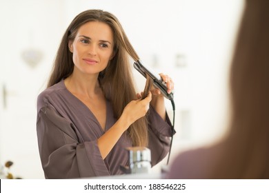 Young Woman Straightening Hair In Bathroom