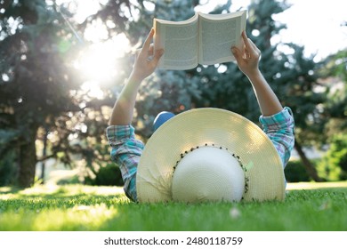 A young woman in a straw hat enjoys spending time reading a book in the park - Powered by Shutterstock