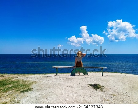 A young woman in straw hat sitting at the seaside on the bench on sunny summer day. girl enjoying an incredible view of the calm blue sea and azure sky. concept of peace and freedom.