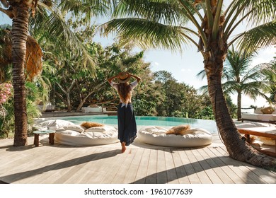 Young woman in straw hat walk near the swimming pool under palm tree. Tropical summer vacation concept
