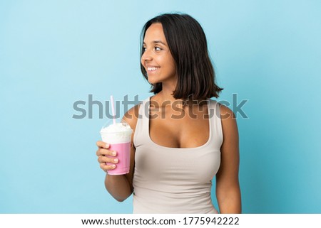 Young woman with strawberry milkshake isolated on blue background looking side