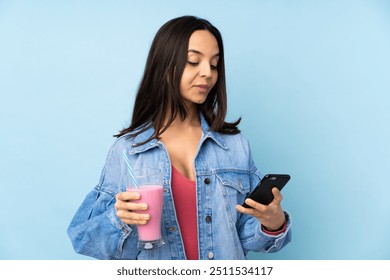 Young woman with strawberry milkshake over isolated blue background holding coffee to take away and a mobile - Powered by Shutterstock