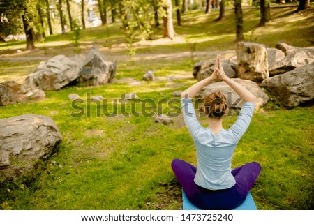 Young Woman  stretching and doing yoga at park. Happy female doing yoga exercise  on a bright morning. Yoga class with woman  doing breath exercise.