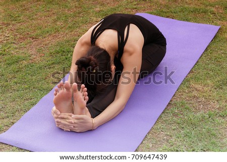 Young woman stretching exercise outdoors.  
is sitting forward bending on the lawn her hands are holding the feets.healthy lifestyle Concept,