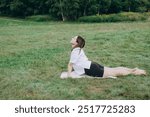 Young Woman Is Stretching Her Back While Practicing Yoga In Cobra Pose On A Mat In The Grass. Cobra Asana