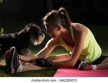 Young woman stretching legs after workout while dog making company