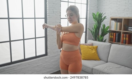 Young woman stretching in modern living room with large windows, white sofa and bookshelf. - Powered by Shutterstock