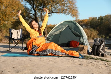 Young Woman Stretching In Sleeping Bag Near Camping Tent Outdoors