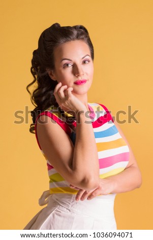 Young woman in striped shirt, with hairdo stands in yellow studio, pin up style