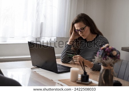 Young woman struggling to pay her bills with credit card due to high inflation.