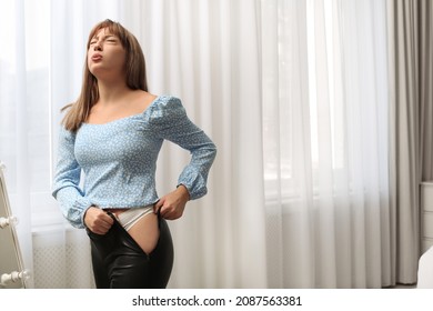 Young woman struggling to put on tight leather pants at home. Space for text