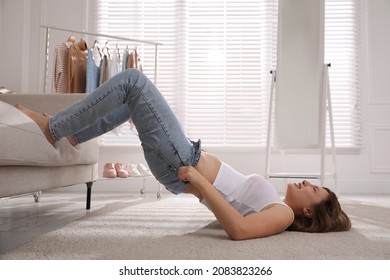 Young Woman Struggling To Squeeze Into Tight Jeans While Lying On Floor At Home