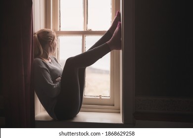 A Young Woman Stuck Indoors Sits On A Window Sill, Gazing Outside And Longing To Be Free.