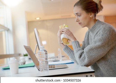 Young Woman Student Eating Sandwich In Front Of Laptop Computer