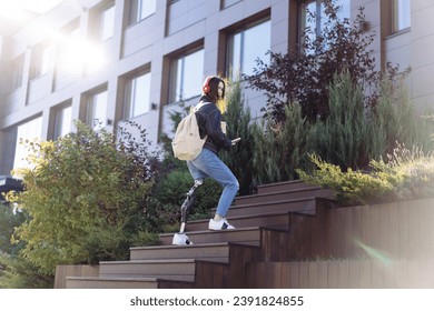 Young woman student with prosthetic leg walking upstairs in city. Disabled woman with prosthetic leg using stairs. Woman with leg prosthesis equipment. - Powered by Shutterstock