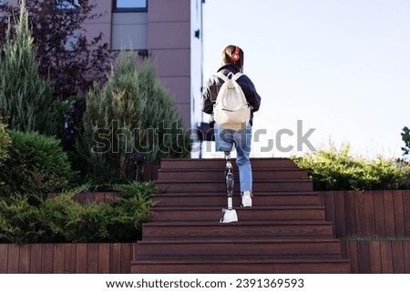 Young woman student with prosthetic leg walking upstairs in city. Disabled woman with prosthetic leg using stairs. Woman with leg prosthesis equipment.
