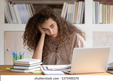 Young Woman Student Sitting At Desk Full With Books Textbooks Looking At Computer Screen To Unfinished Homework Feels Tired Bored And Unmotivated, Girl Loaded With Tasks, Work Backlog Overflow Concept