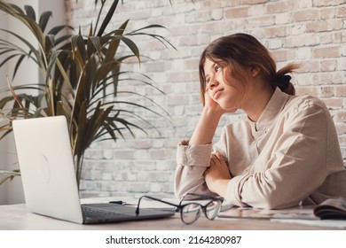 Young Woman Student Sitting At Desk Full With Books Textbooks Looking At Computer Screen To Unfinished Homework Feels Tired Bored And Unmotivated, Girl Loaded With Tasks, Work Backlog Overflow Concept