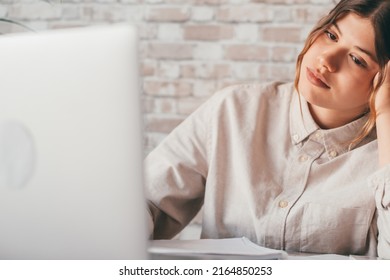 Young Woman Student Sitting At Desk Full With Books Textbooks Looking At Computer Screen To Unfinished Homework Feels Tired Bored And Unmotivated, Girl Loaded With Tasks, Work Backlog Overflow Concept