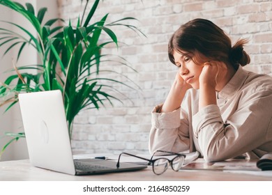 Young Woman Student Sitting At Desk Full With Books Textbooks Looking At Computer Screen To Unfinished Homework Feels Tired Bored And Unmotivated, Girl Loaded With Tasks, Work Backlog Overflow Concept