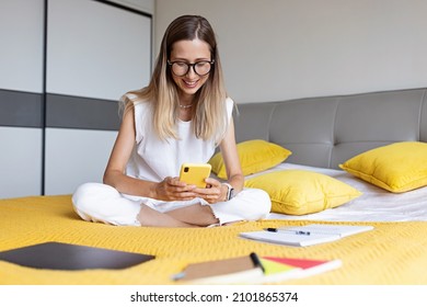 Young Woman student studying online via video chat. Stylish freelancer works from home. Blogger working from home office. Millennial business woman lying on bed in modern apartment. 