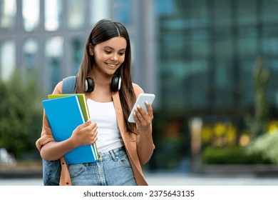 Young woman student texting on smartphone at campus, copy space. Positive cheerful lady with backpack and notebooks in her hand walking by street, using phone, copy space. Communication - Powered by Shutterstock