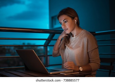 Young Woman Student Using Laptop While Listening To Music At Night. High ISO Image.