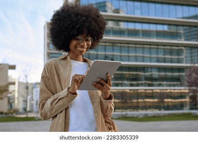 A young woman student using touchscreen of pc tablet standing in university campus. An African American cheerful female business freelancer entrepreneur using app project for online work outdoors. - Powered by Shutterstock