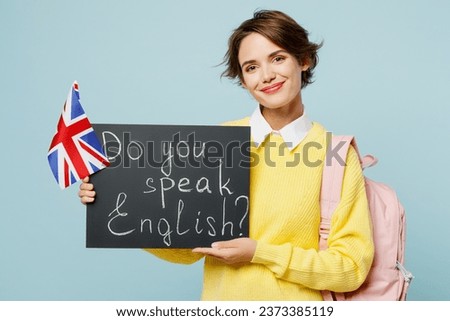Young woman student wear casual clothes sweater backpack bag hold British flag card sign with do you speak English title text isolated on plain blue background. High school university college concept