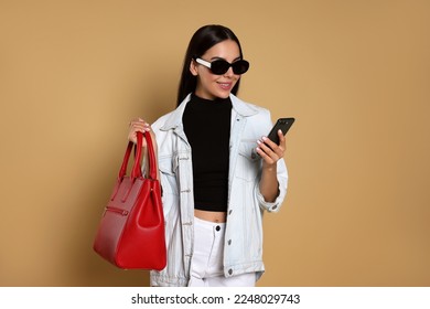 Young woman with stylish bag using smartphone on beige background - Powered by Shutterstock