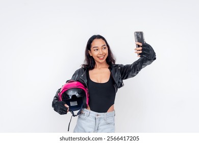 A young woman in stylish motorcycle gear taking a selfie, helmet in hand. Isolated on a white background. - Powered by Shutterstock