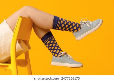 Young woman in stylish sneakers sitting on chair against yellow background