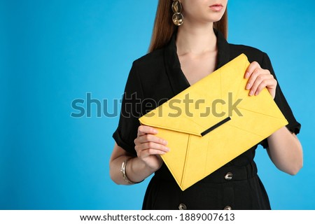 Young woman with stylish yellow bag on light blue background, closeup. Space for text
