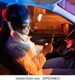 Young Woman Suffer From Smartphone Addiction, Spend Day And Night In Social Media. African Girl Sit In Dark Car Holding Mobile Phone In Hand, Texting, Scrolling Websites And Communicating Via Internet